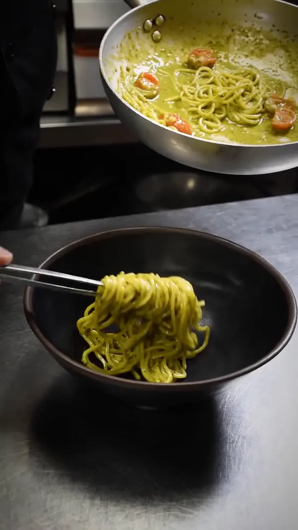 Pasta servida desde la sartén a un cuenco negro.