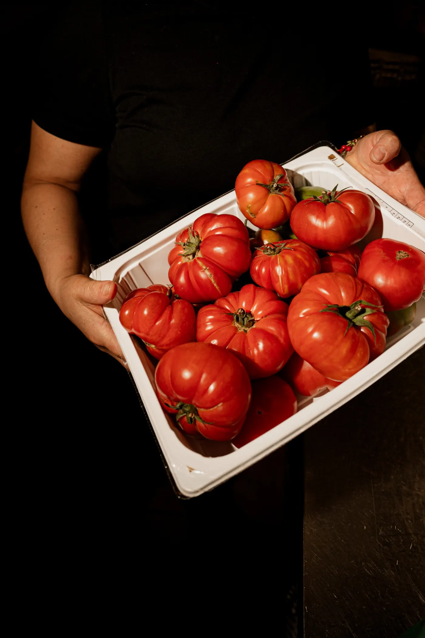 Unas manos sostienen una bandeja blanca llena de tomates rojos.